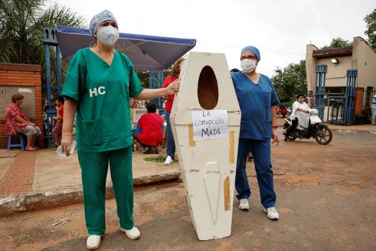 Hospital de Clinicas'ın sağlık çalışanları, San Lorenzo, Paraguay'da sağlık sisteminin çökmesini protesto ederken 'Yolsuzluk öldürüyor' yazan sahte bir tabutla ayakta duruyorlar Cesar Olmedo.jpg