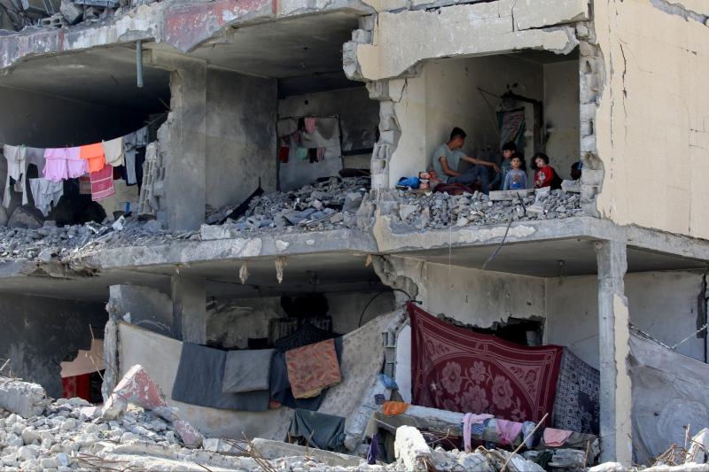 Filistinli bir adam ve çocukları, İsrail'in hava saldırısının Refah'taki bir konutu hedef almasının ardından tahrip olmuş odada oturuyor
