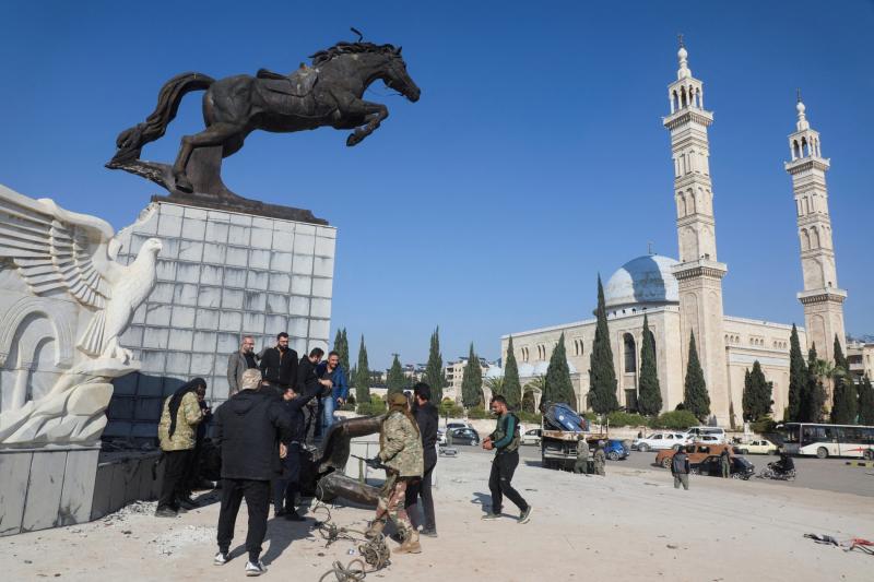 Suriyeliler, Halep'in merkezinde Basil Hafız Esad'ın heykelini devirdikten sonra bir at heykelinin önünden geçiyor, 29 Kasım 2024 / Fotoğraf: Reuters