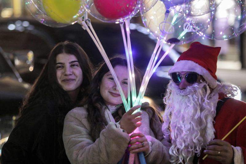 Suriye'nin güneyindeki Suveyda şehrinde ışıklı balonlar tutan genç kızlarla poz veren Noel Baba kılığına girmiş bir adam, 29 Aralık 2024 / Fotoğraf: AFP