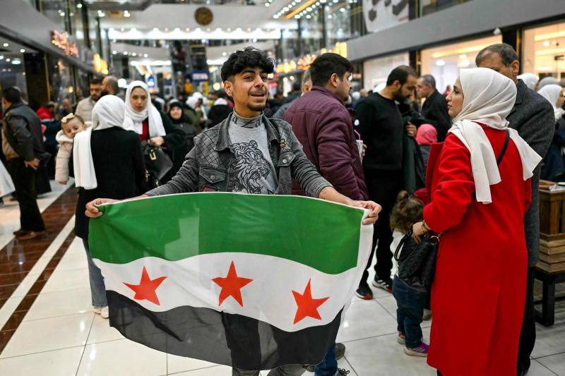 Suriye'nin kuzeyindeki İdlib'e bağlı Sarmada yakınlarında bulunan ed-Dana semtinde bir alışveriş merkezinde devrim bayrağı tutan genç, 13 Aralık 2024 / Fotoğraf: AFP